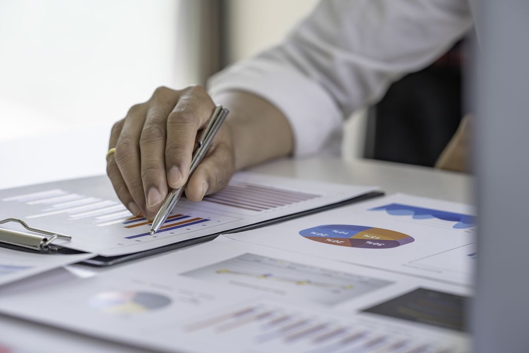 Hand mit Stift über ausgedruckten Auswertungen